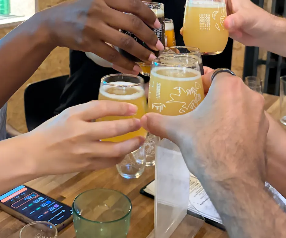 Six hands clinking beer tasters at a Rounds table